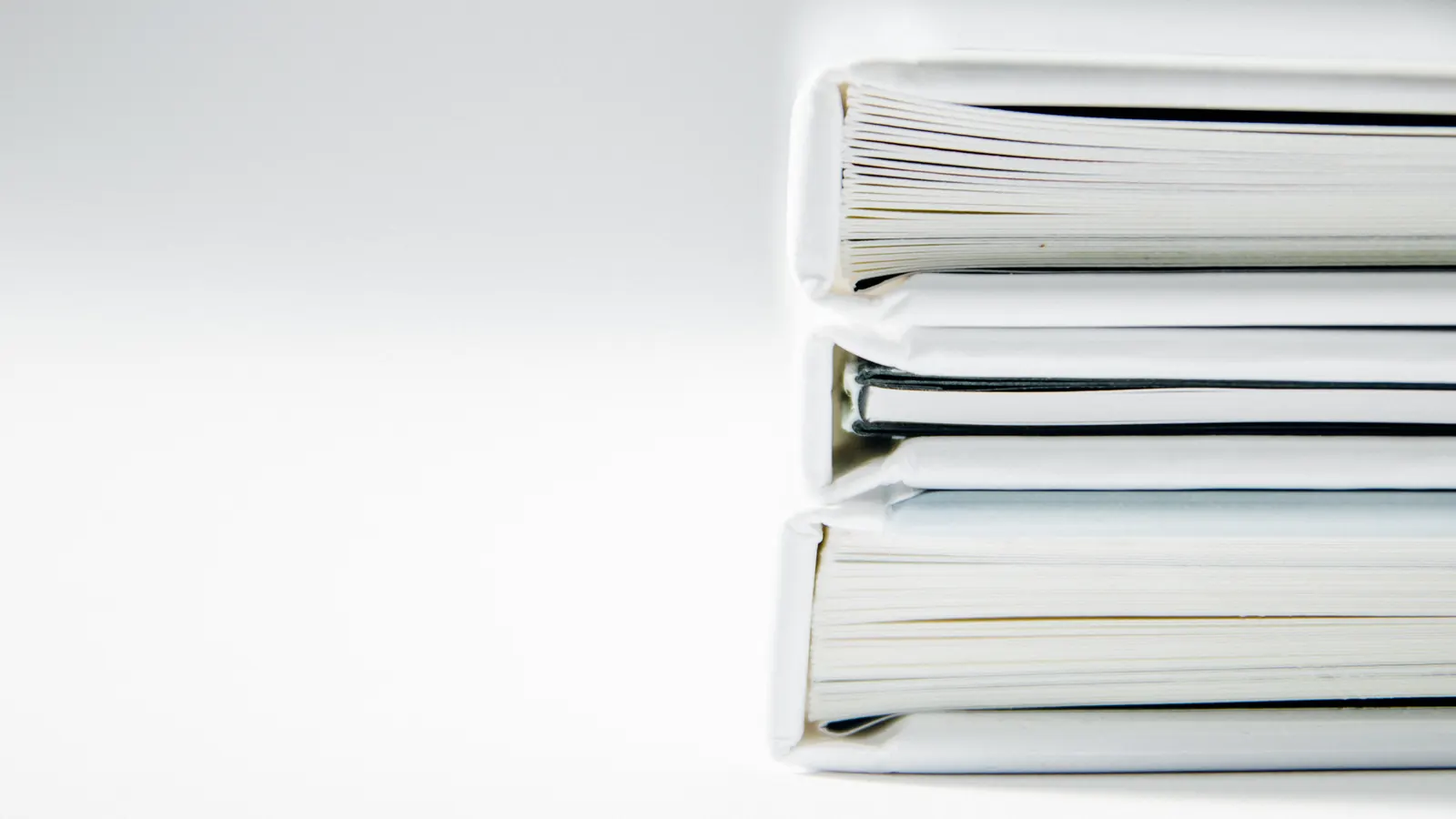 A stack of white ring binders on a white surface, seen from the side