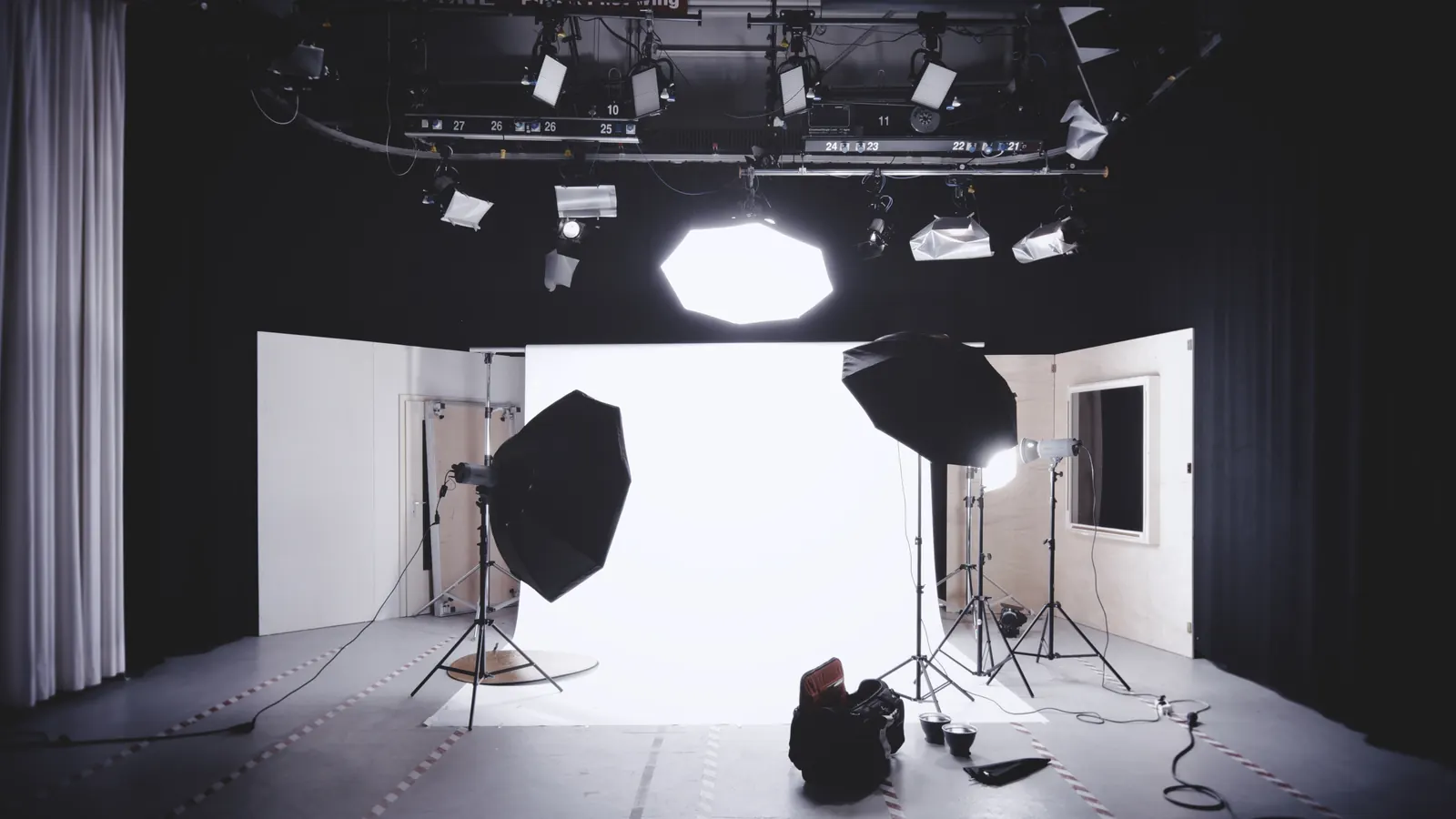 An empty photo studio with softbox lights, light stands and a white backdrop under a lighting rig