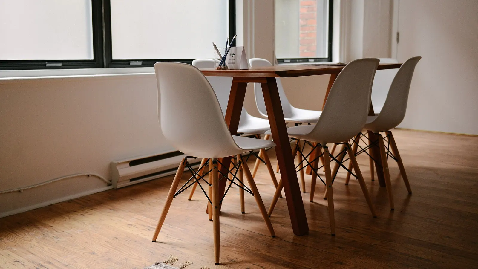 A small meeting table with six white chairs and a cup of pens in a bright, empty office
